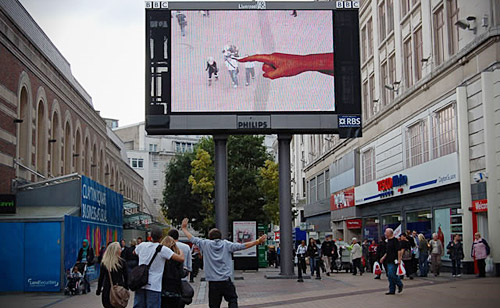 Billboard prods and miniaturises passing Scousers